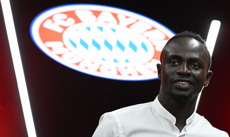 Sadio Mane poses in front of the Bayern Munich logo.
