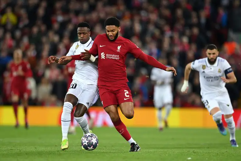 Joe Gomez of Liverpool runs with the ball whilst under pressure from Vinicius Junior of Real Madrid.